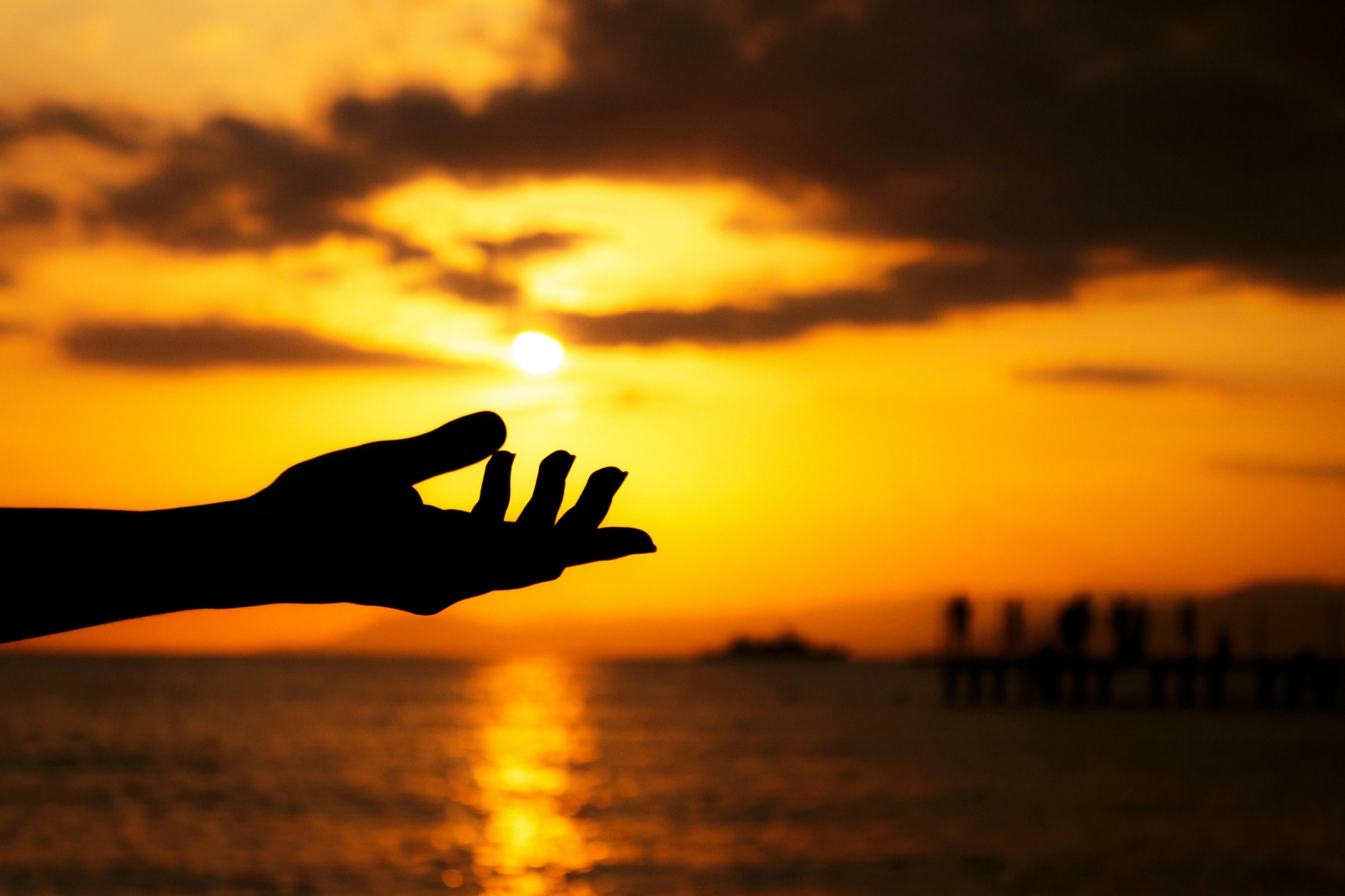 Hand reaching toward the sun over the water at sunset